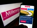 Person holding cellphone with webpage of Polish financial company Bank Millennium S.A. on screen in front of logo.