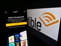 Person holding cellphone with webpage of US audiobook company Audible Inc. on screen in front of logo.