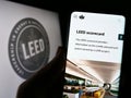 Person holding cellphone with webpage of US green building certification LEED on screen in front of logo.