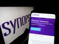 Person holding cellphone with webpage of US technology company Synopsys Inc. on screen in front of logo.