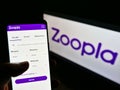 Person holding cellphone with website of British real estate platform Zoopla Limited on screen in front of logo.