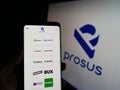Person holding cellphone with website of Dutch investment company Prosus N.V. on screen in front of business logo.