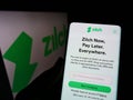 Person holding cellphone with website of fintech Zilch Technology Limited (PayZilch) on screen in front of logo.