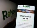 Person holding cellphone with website of Indian company ReNew Energy Global plc on screen in front of logo.