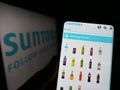 Person holding cellphone with website of Japanese beverage company Suntory Holdings K.K. on screen with logo.