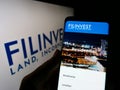 Person holding cellphone with website of real estate company Filinvest Land Inc. (FLI) on screen with logo.