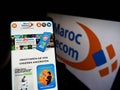 Person holding cellphone with website of company Maroc Telecom (IAM) on screen with logo.