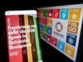 Person holding cellphone with website of UN Sustainable Development Goals (SDG) on screen in front of logo.