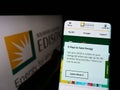 Person holding cellphone with website of US company Southern California Edison (SCE) on screen in front of logo.