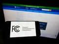 Person holding cellpohone with seal of American agency Federal Communications Commission (FCC) on screen with website.