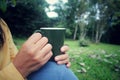 Person holding cup of tea or coffee in hands. Woman with glass of water in hand. On green nature park background. Royalty Free Stock Photo