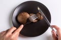 A person is holding a cutlery fork and knife and cuts a raw jersey cow mushroom on a black plate on a white background Royalty Free Stock Photo