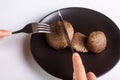 A person is holding a cutlery fork and knife and cuts a raw jersey cow mushrooms on a black plate on a white background Royalty Free Stock Photo