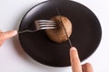 A person is holding a cutlery fork and knife and cutting a raw one jersey cow mushroom on a black plate on a white Royalty Free Stock Photo