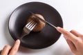 A person is holding a cutlery fork and knife and cutting a raw one jersey cow mushroom on a black plate on a white Royalty Free Stock Photo