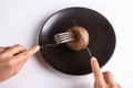 A person is holding a cutlery fork and knife and cutting a raw one jersey cow mushroom on a black plate on a white Royalty Free Stock Photo