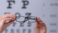 Person holding eyeglasses against eyechart, vision disorder prevention, clinic