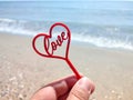 Person holding in fingers hand a stick in shape of red heart and word Love Royalty Free Stock Photo