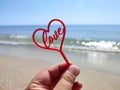 Person holding in fingers hand stick in shape red heart and word Love Royalty Free Stock Photo