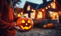 A person holding a glowing pumpkin with scary carved face outside a house