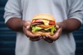 person holding a greasy cheeseburger with lettuce