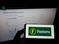 Person holding mobile phon with logo of British estate agency Foxtons Group plc on screen in front of business web page.