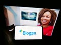 Person holding mobile phone with business logo of American biotechnology company Biogen Inc. on screen in front of web page.