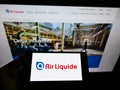 Person holding mobile phone with business logo of French chemical company Air Liquide SA on screen in front of webpage.