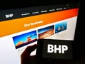 Person holding mobile phone with business logo of mining company BHP Group on screen in front of web page.