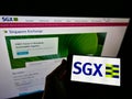 Person holding mobile phone with business logo of stock exchange Singapore Exchange (SGX) on screen with web page.