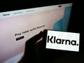 Person holding mobile phone with business logo of Swedish payment company Klarna Bank AB on screen in front of web page.