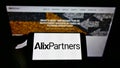 Person holding mobile phone with business logo of US consulting firm AlixPartners LLP on screen in front of company website.