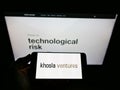 Person holding mobile phone with business logo of US venture capital firm Khosla Ventures LLC on screen in front of web page.