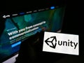 Person holding mobile phone with business logo of US video game company Unity Software Inc. on screen in front of web page.