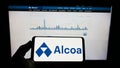 Person holding mobile phone with logo of American aluminium company Alcoa Corporation on screen in front of web page.