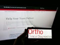 Person holding mobile phone with logo of American company Ortho Clinical Diagnostics on screen in front of business web page.