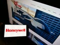 Person holding mobile phone with logo of American conglomerate Honeywell International Inc. on screen in front of web page.