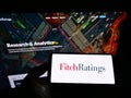 Person holding mobile phone with logo of American credit rating agency Fitch Ratings Inc. on screen in front of web page.