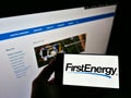 Person holding mobile phone with logo of American electric utility company FirstEnergy Corp. on screen in front of web page. Royalty Free Stock Photo