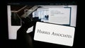 Person holding mobile phone with logo of American investment company Harris Associates LP on screen in front of web page.