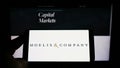 Person holding mobile phone with logo of American investment firm Moelis and Company on screen in front of web page.