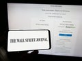Person holding mobile phone with logo of American newspaper The Wall Street Journal on screen in front of web page.