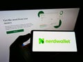 Person holding mobile phone with logo of American personal finance company NerdWallet Inc. on screen in front of web page.