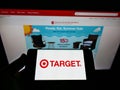 Person holding mobile phone with logo of American retail company Target Corporation on screen in front of web page.