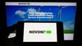 Person holding mobile phone with logo of Australian battery company Novonix Limited on screen in front of business web page.