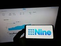 Person holding mobile phone with logo of Australian Nine Entertainment Co. Holdings Limited on screen in front of web page.