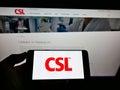 Person holding mobile phone with logo of Australian pharmaceuticals company CSL Limited on screen in front of web page.
