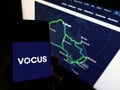 Person holding mobile phone with logo of Australian telecommunications company Vocus Group on screen in front of web page.