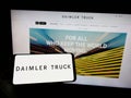 Person holding mobile phone with logo of automotive company Daimler Truck Holding AG on screen in front of web page.