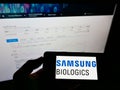 Person holding mobile phone with logo of biotechnology company Samsung Biologics Co. Ltd. on screen in front of webpage.